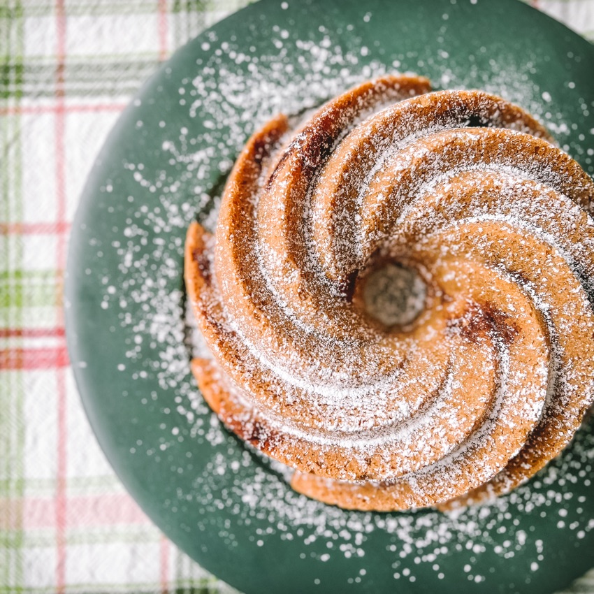 Spiced hazelnut and lingonberry bundt cake on platter with confectioner's sugar